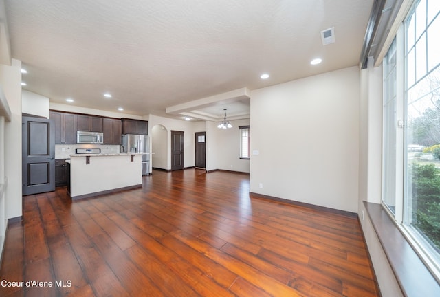 unfurnished living room featuring visible vents, baseboards, an inviting chandelier, recessed lighting, and dark wood-style flooring