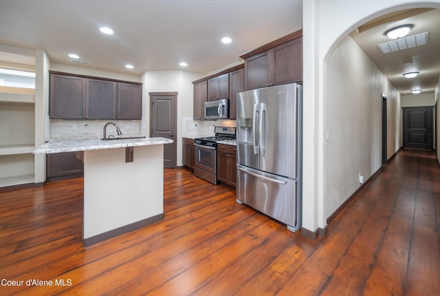 kitchen featuring visible vents, arched walkways, dark brown cabinets, appliances with stainless steel finishes, and a kitchen breakfast bar