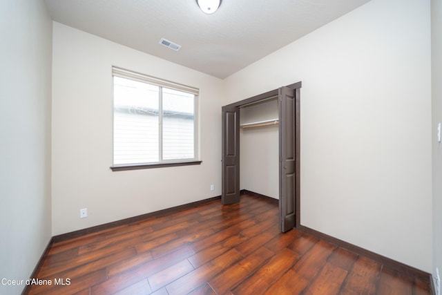 unfurnished bedroom with dark wood finished floors, baseboards, visible vents, and a closet