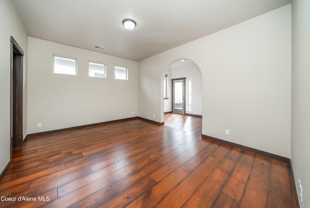 spare room with dark wood finished floors, arched walkways, visible vents, and baseboards