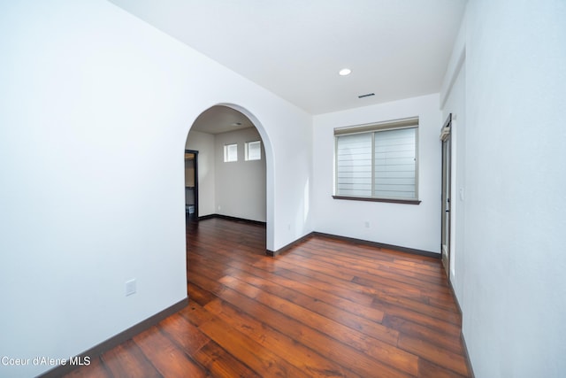 empty room featuring visible vents, dark wood finished floors, recessed lighting, arched walkways, and baseboards