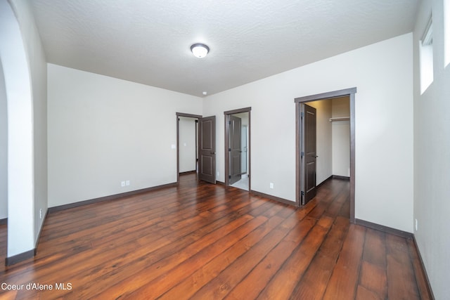 unfurnished bedroom with a walk in closet, baseboards, a textured ceiling, and dark wood finished floors