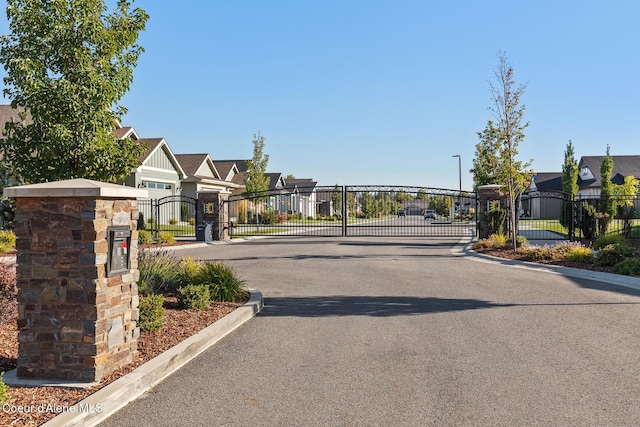 view of street with curbs, a gated entry, a gate, and a residential view