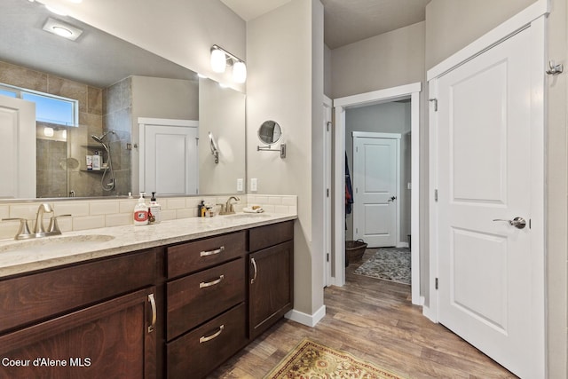 bathroom featuring double vanity, a sink, a tile shower, and wood finished floors