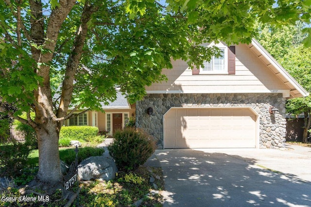 obstructed view of property featuring a garage, concrete driveway, and stone siding