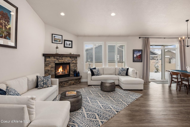 living room featuring a textured ceiling, a stone fireplace, recessed lighting, a notable chandelier, and dark wood finished floors