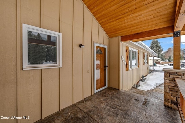 snow covered property entrance with a patio area, fence, and board and batten siding