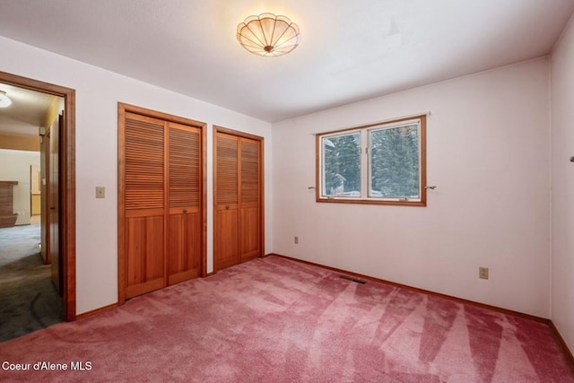 unfurnished bedroom featuring multiple closets, light carpet, visible vents, and baseboards