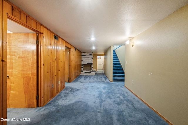 finished below grade area featuring carpet, visible vents, wooden walls, baseboards, and stairs