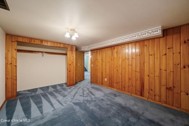 unfurnished bedroom with dark colored carpet, a closet, visible vents, and wooden walls