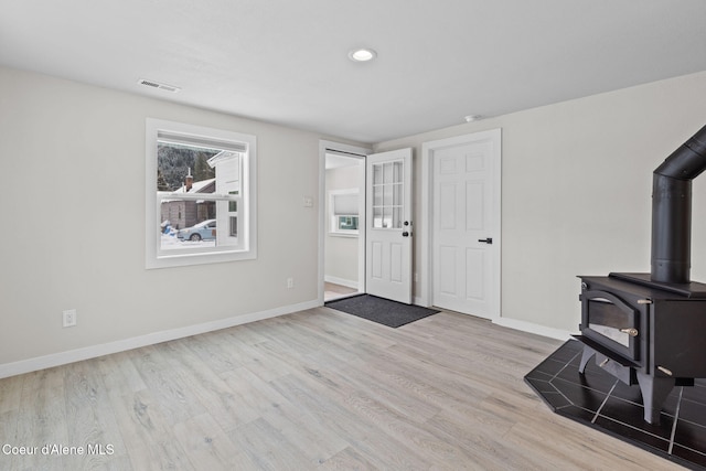 foyer entrance featuring light wood-style flooring, recessed lighting, visible vents, baseboards, and a wood stove