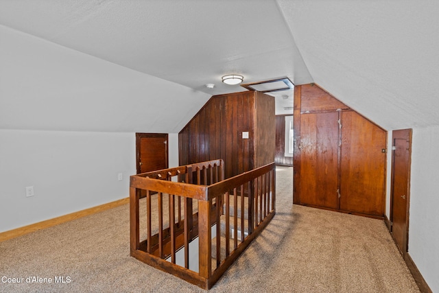 additional living space featuring light colored carpet, vaulted ceiling, wooden walls, and baseboards