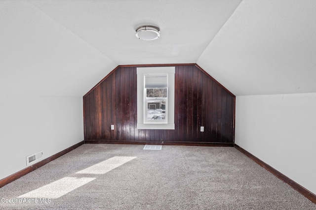 additional living space with lofted ceiling, light colored carpet, wood walls, visible vents, and baseboards