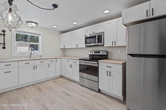 kitchen featuring light wood finished floors, stainless steel appliances, light countertops, white cabinetry, and a sink