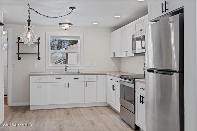 kitchen with white cabinets, stainless steel appliances, light countertops, pendant lighting, and a sink