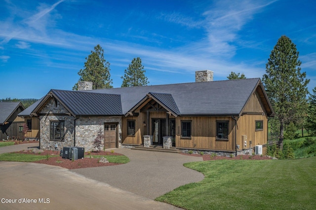 view of front of home with a chimney, a standing seam roof, metal roof, driveway, and a front lawn