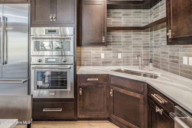 kitchen with light stone counters, stainless steel appliances, tasteful backsplash, dark brown cabinetry, and a sink