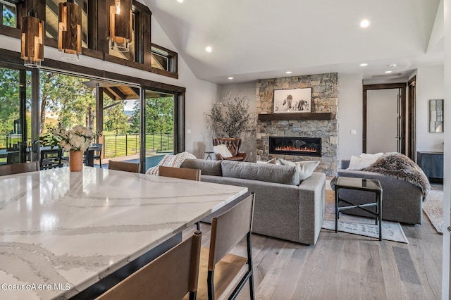 living area with lofted ceiling, a stone fireplace, light wood finished floors, and recessed lighting