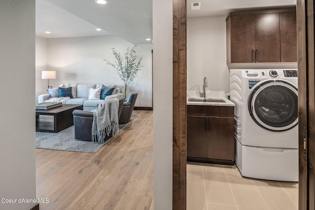 washroom featuring a sink, visible vents, light wood-type flooring, cabinet space, and washer / dryer