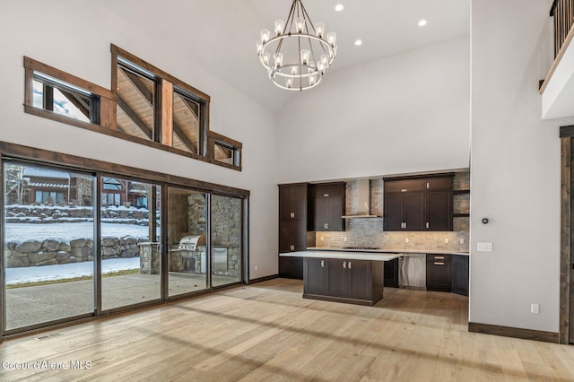 kitchen featuring a center island, light countertops, dark brown cabinets, wall chimney range hood, and pendant lighting