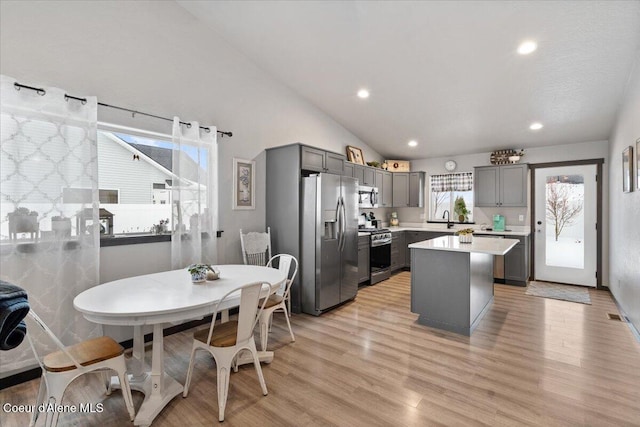 kitchen with light wood finished floors, a center island, stainless steel appliances, light countertops, and gray cabinetry