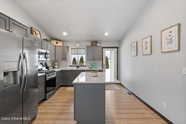 kitchen with light countertops, light wood-style flooring, gray cabinetry, appliances with stainless steel finishes, and a kitchen island