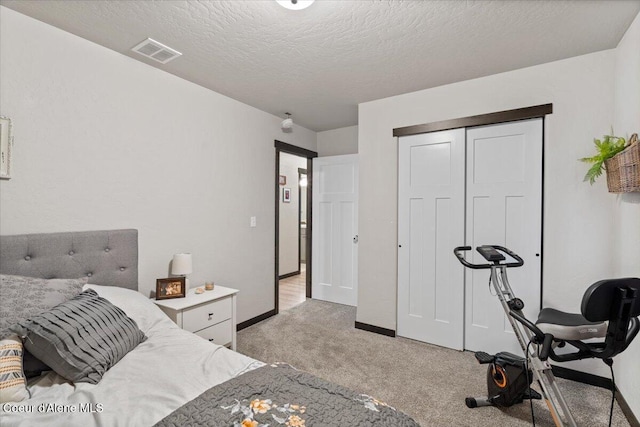 bedroom featuring baseboards, visible vents, light colored carpet, a textured ceiling, and a closet