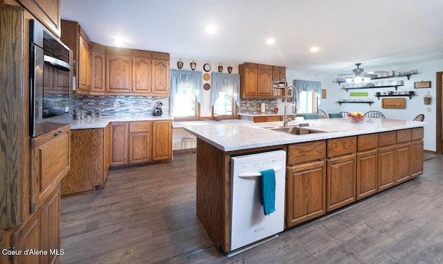 kitchen with a sink, brown cabinets, dishwasher, dark wood finished floors, and a center island with sink