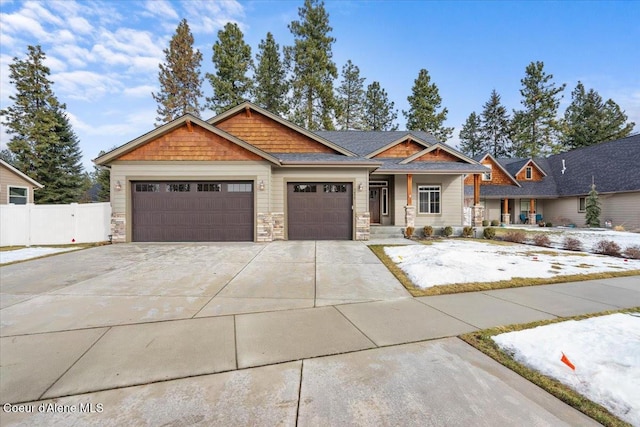 craftsman-style house with a garage, stone siding, driveway, and fence