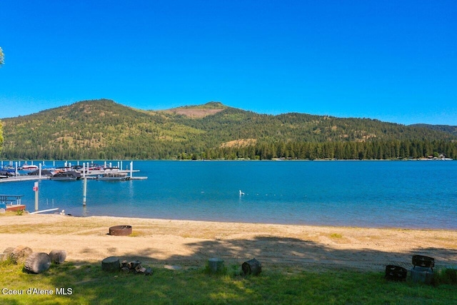 view of water feature with a dock, a mountain view, and a view of trees