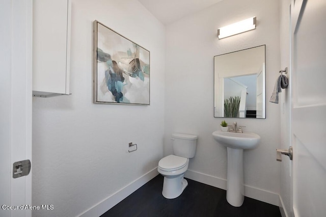 half bath featuring toilet, baseboards, and a sink