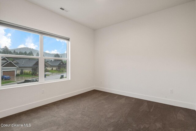 unfurnished room with dark carpet, visible vents, and baseboards