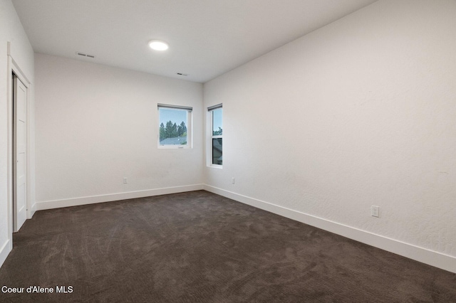 unfurnished room with dark colored carpet, visible vents, and baseboards