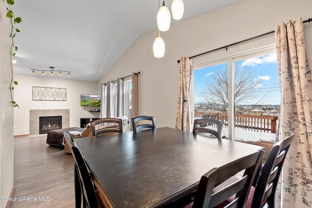 dining room with a tile fireplace, a healthy amount of sunlight, vaulted ceiling, and wood finished floors