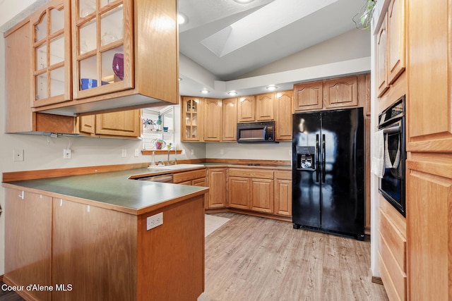 kitchen with light wood finished floors, glass insert cabinets, a sink, vaulted ceiling with skylight, and black appliances