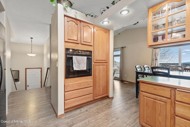 kitchen with light wood-style flooring, glass insert cabinets, hanging light fixtures, light countertops, and black oven