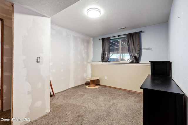 unfurnished room with carpet, visible vents, and a textured ceiling