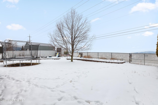 yard layered in snow featuring a trampoline and fence