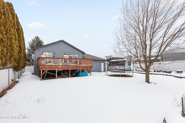 snow covered rear of property with a trampoline, fence, and a deck