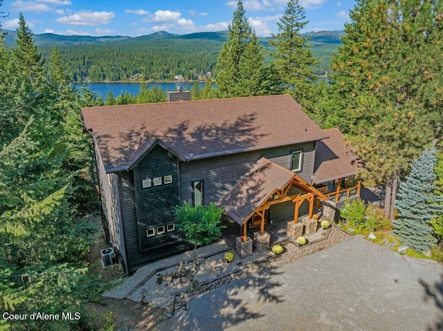 rustic home featuring a chimney, a water and mountain view, central AC, driveway, and a forest view