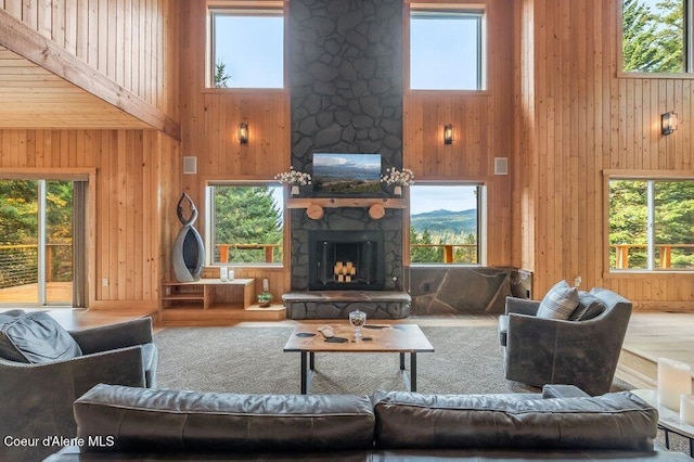 living area with a healthy amount of sunlight, a fireplace, wood walls, and a high ceiling