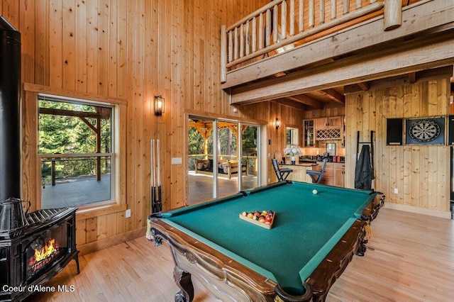 recreation room with a wood stove, wood walls, light wood-style floors, and beam ceiling