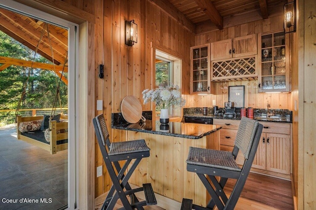 kitchen with wooden ceiling, a breakfast bar area, glass insert cabinets, beamed ceiling, and wood walls