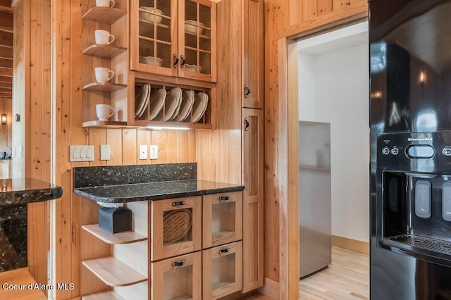 kitchen featuring open shelves, black fridge, dark stone countertops, and glass insert cabinets