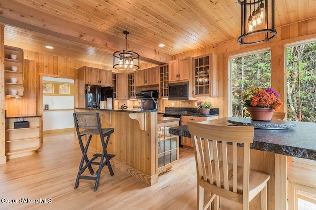 kitchen with light wood finished floors, dark countertops, wooden ceiling, a breakfast bar, and black fridge