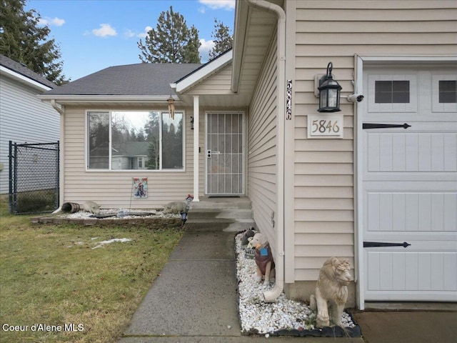 view of exterior entry with a lawn and roof with shingles