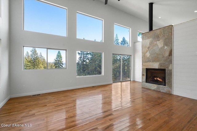 unfurnished living room with visible vents, a high ceiling, light wood-type flooring, baseboards, and a tile fireplace