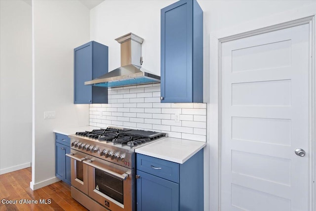 kitchen featuring range with two ovens, light countertops, blue cabinetry, and wall chimney exhaust hood