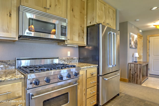 kitchen with premium appliances, light stone counters, decorative backsplash, light brown cabinets, and baseboards