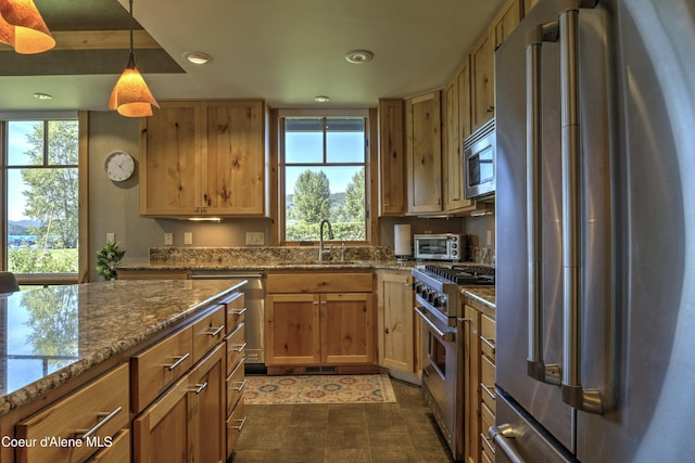 kitchen featuring stone counters, pendant lighting, high end appliances, recessed lighting, and a sink